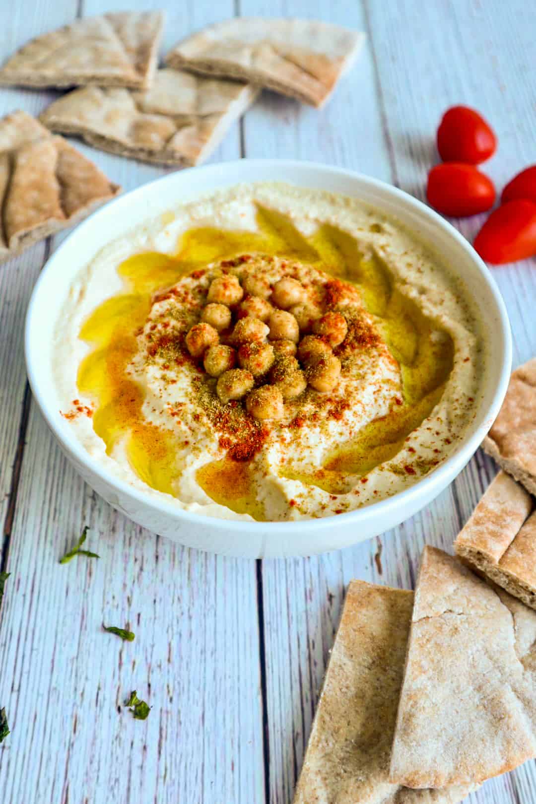 A bowl of hummus with chick peas, paprika, cumin and olive oil on top. side of sliced pita bread.