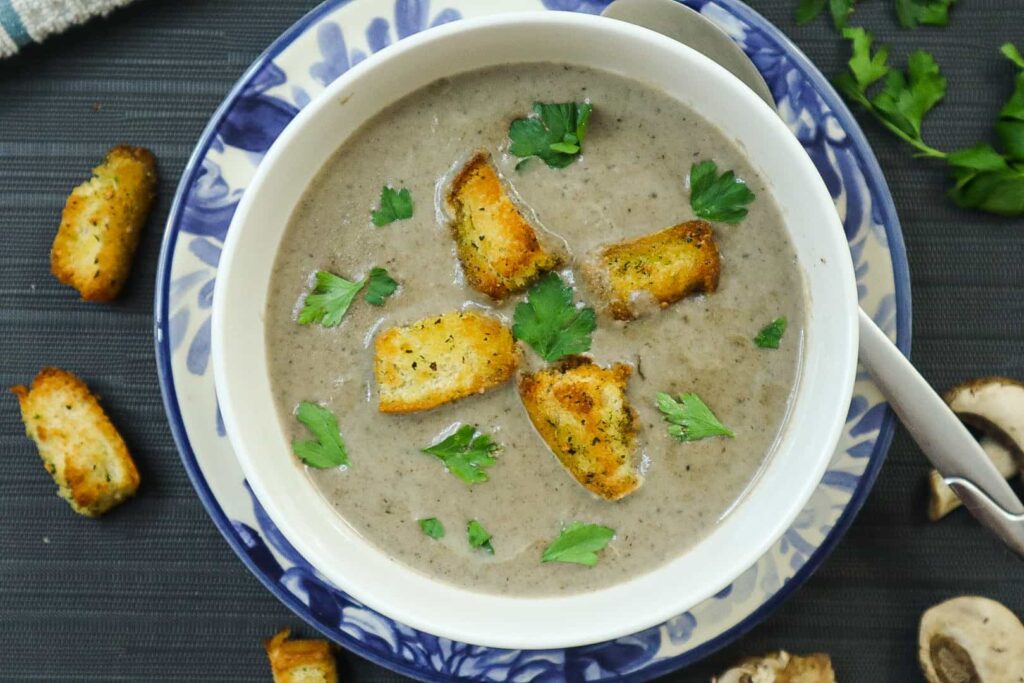 A bowl of creamy mushroom soup with croutons and parsley as garnish