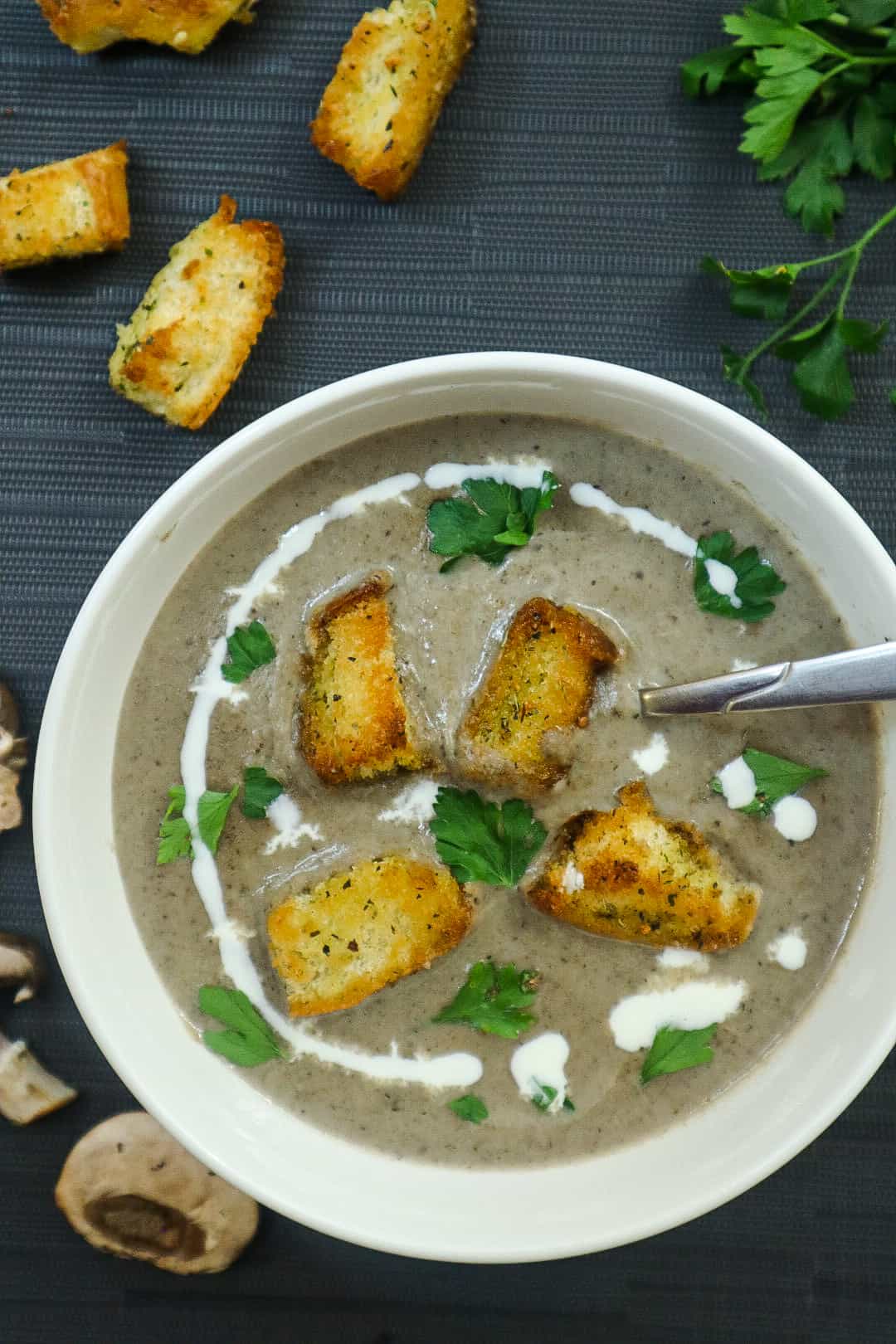 A bowl of mushroom soup, some homemade croutons on top and parsley.