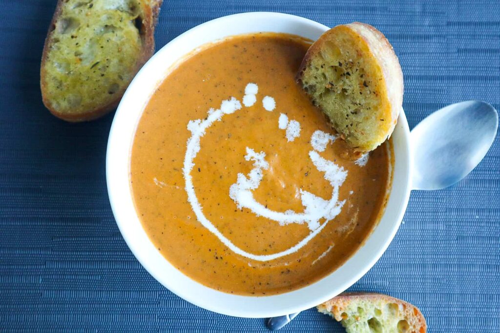 A bowl of Tomato Soup with toasted bread dipped in it 