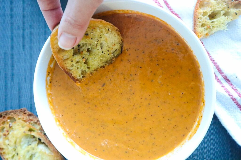 A bowl of creamy tomato soup with a piece of bread dipped in it
