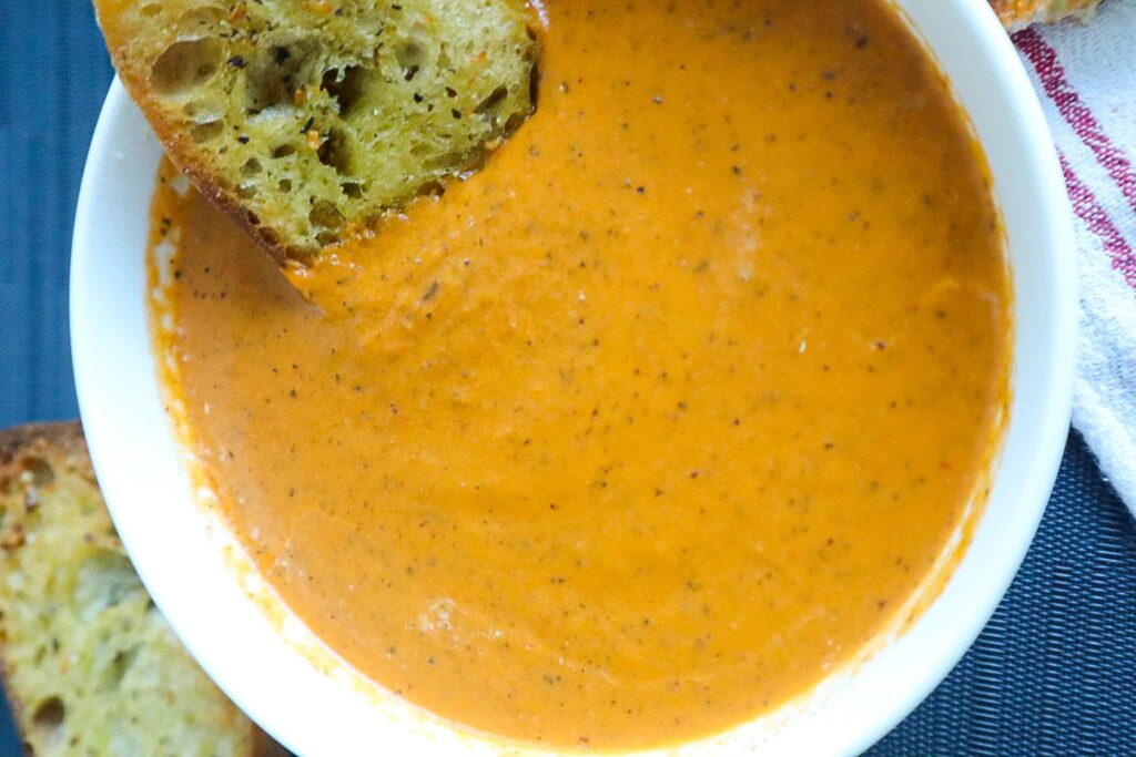 A bowl of tomato soup with bread dipped in it