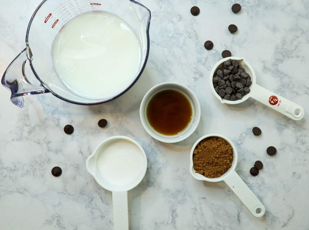 Homemade Hot chocolate ingredients in measuring cups. Milk, sugar, Cocoa powder, chocolate chips and vanilla extract.