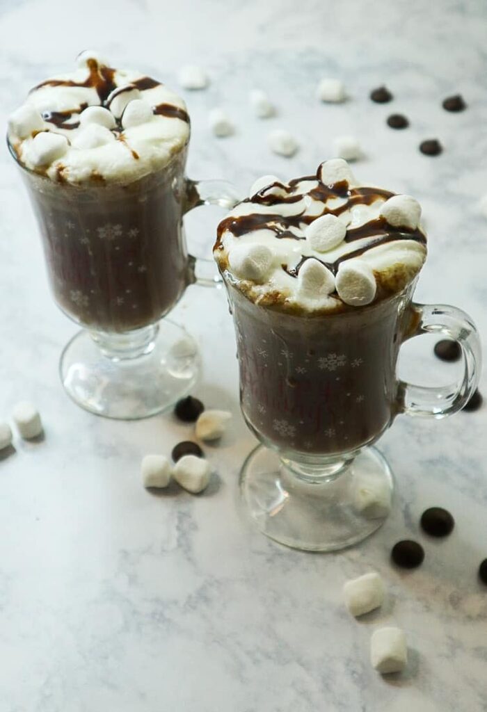 Two glasses of homemade hot chocolate with marshmallows and dark chocolate chips on top. 
