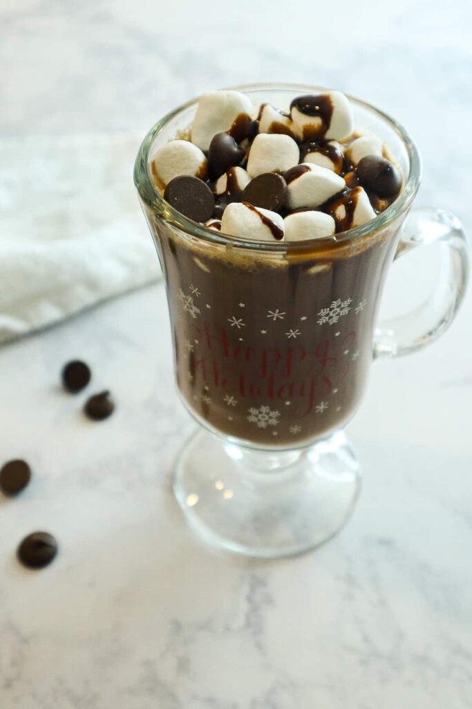 A glass of homemade hot chocolate with marshmallows and dark chocolate chips on top. 