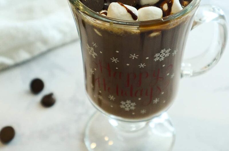 A glass of hot chocolate with marshmallows and dark chocolate chips on top.