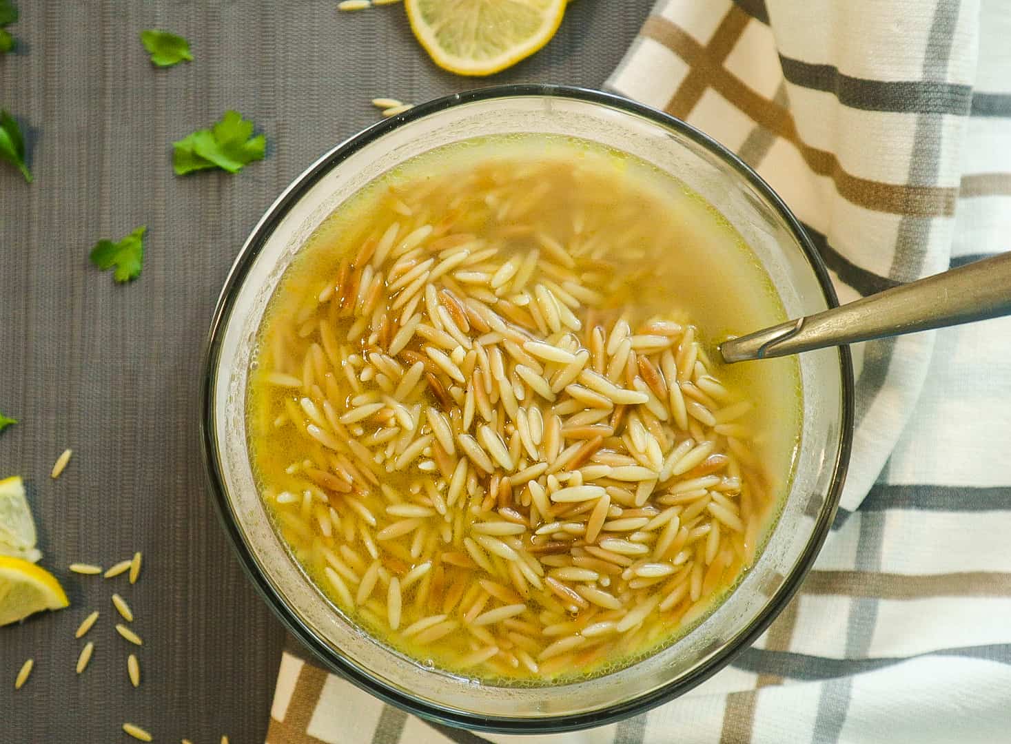 A bowl of orzo soup with slice of lemon on the side.