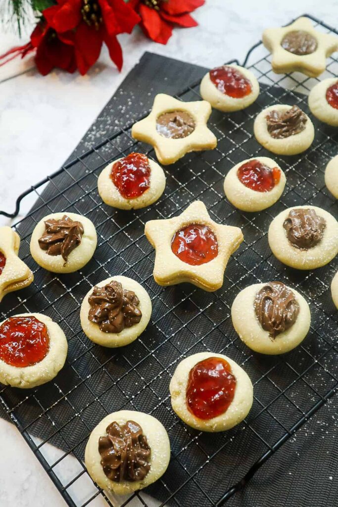 A thumbprint cookies filled with jam and nutella on a sheet rack 