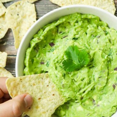 A bowl of guacamole with a tortilla chips dipped in.