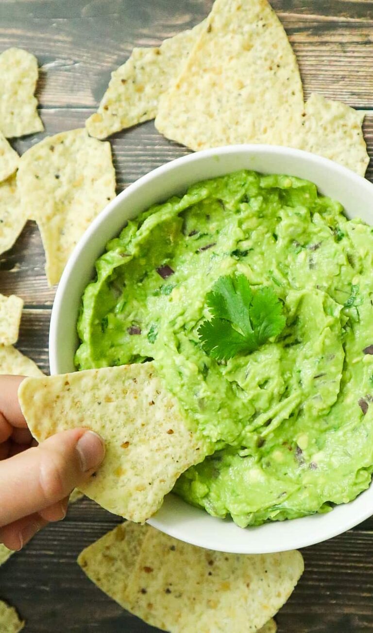 A bowl of guacamole with a tortilla chips dipped in.