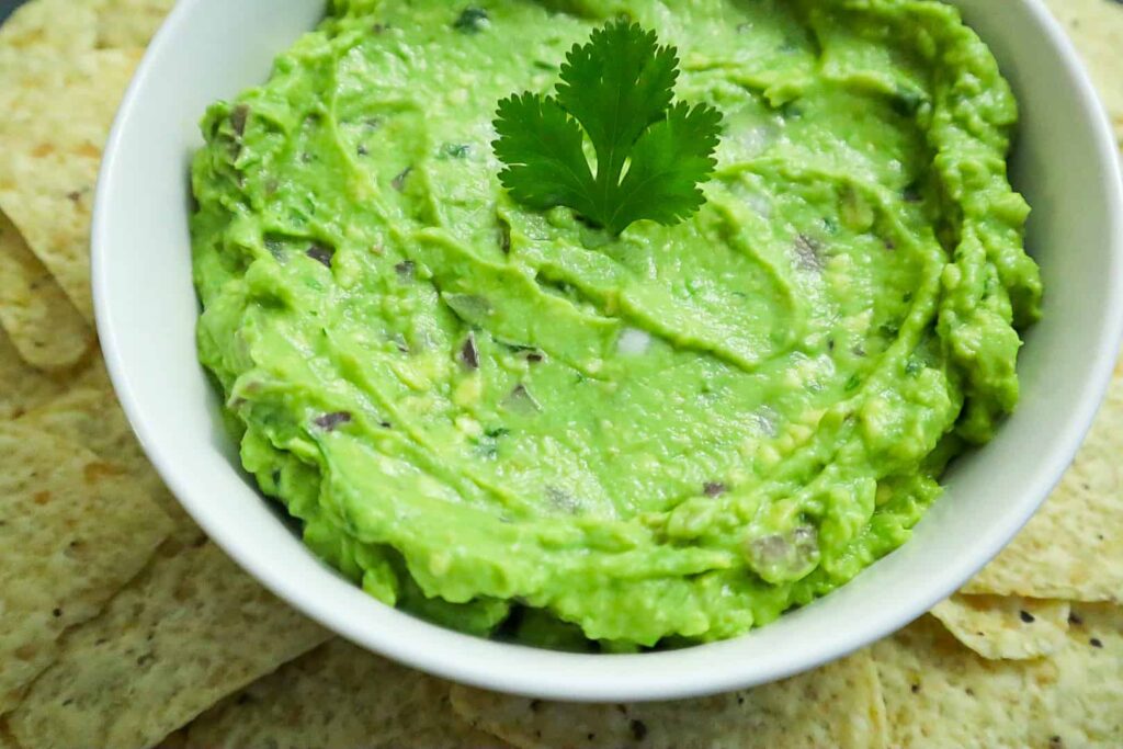 A bowl of Guacamole with tortilla chips on the side