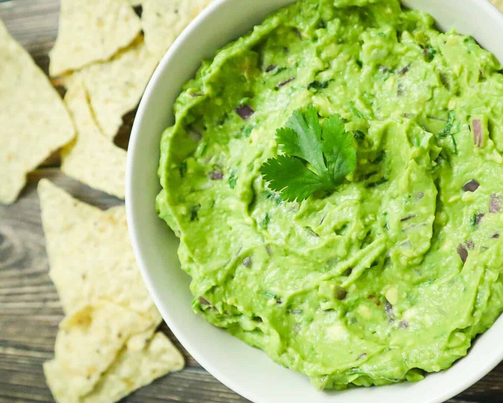 A bowl of best Guacamole recipe with tortilla chips on the side