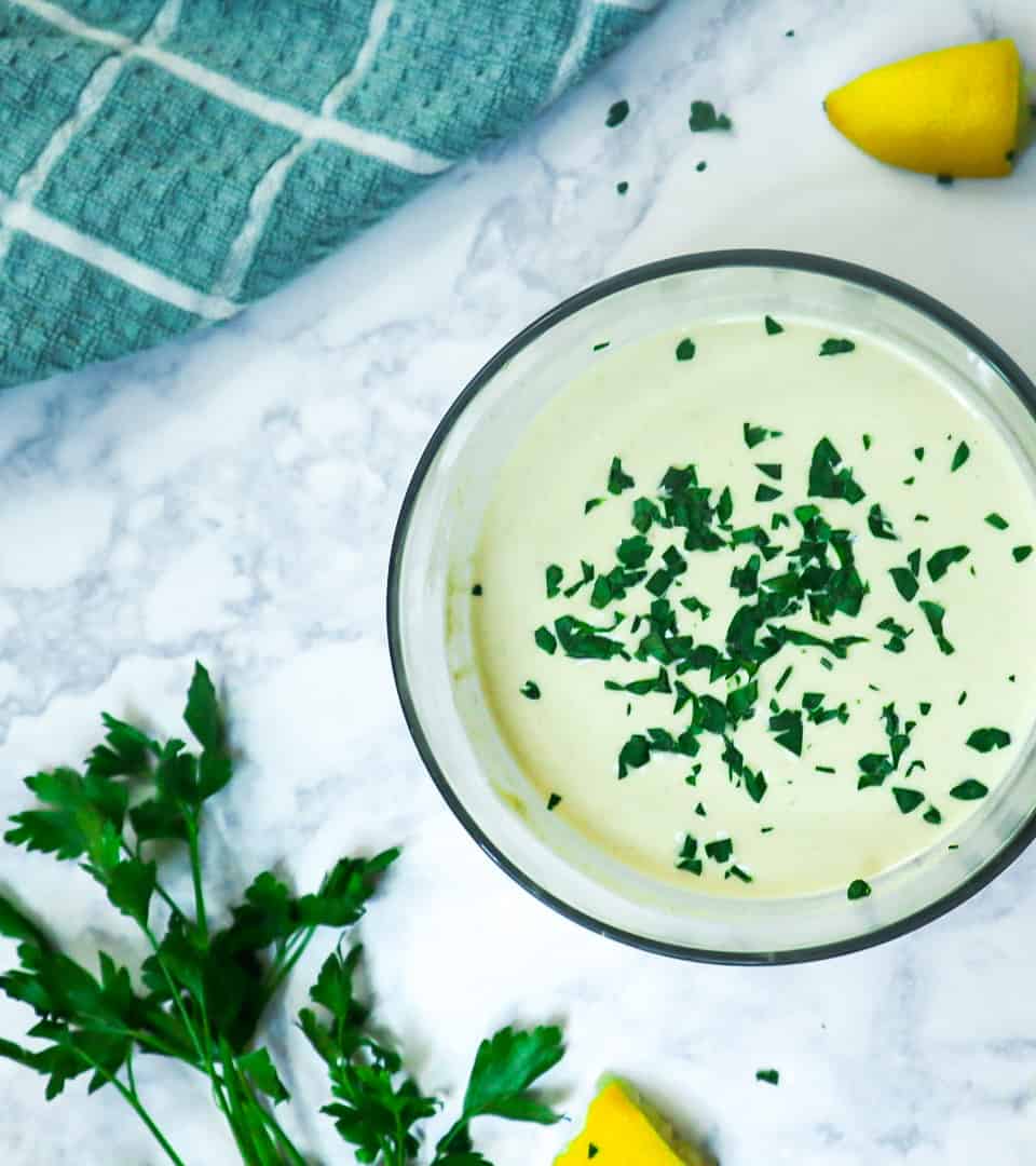 A bowl of tahini sauce topped with chopped parsley as a garnish.