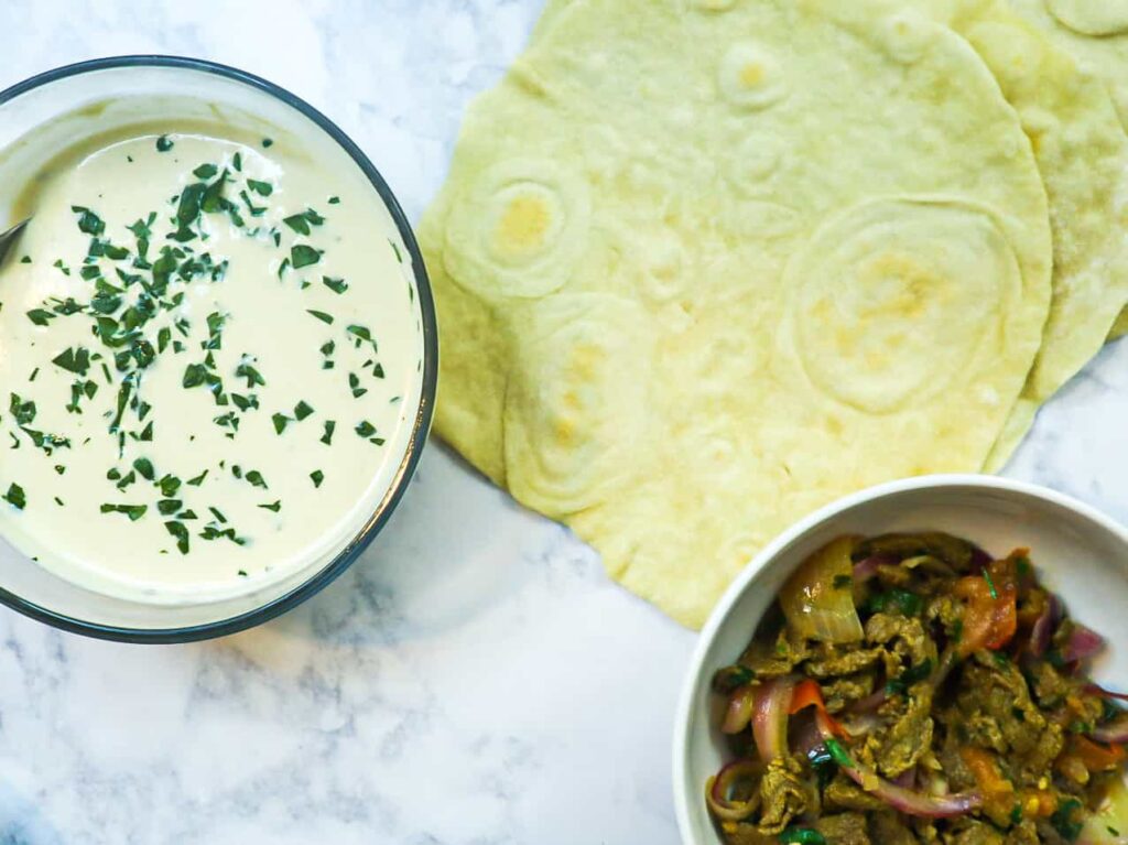 a Bowl of tahini with parsley as a garnish with homemade pita bread and a bowl of beef shawarma 