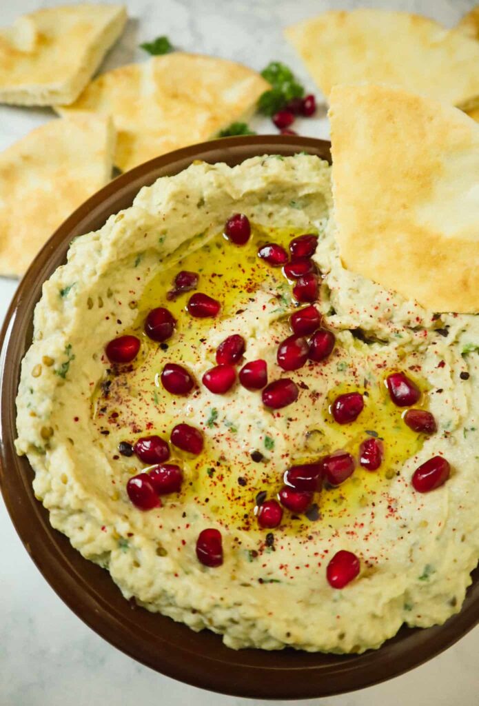 A bowl of a baba ganoush, pomegranate seeds, olive oil, sumac and pieces of pita bread 
