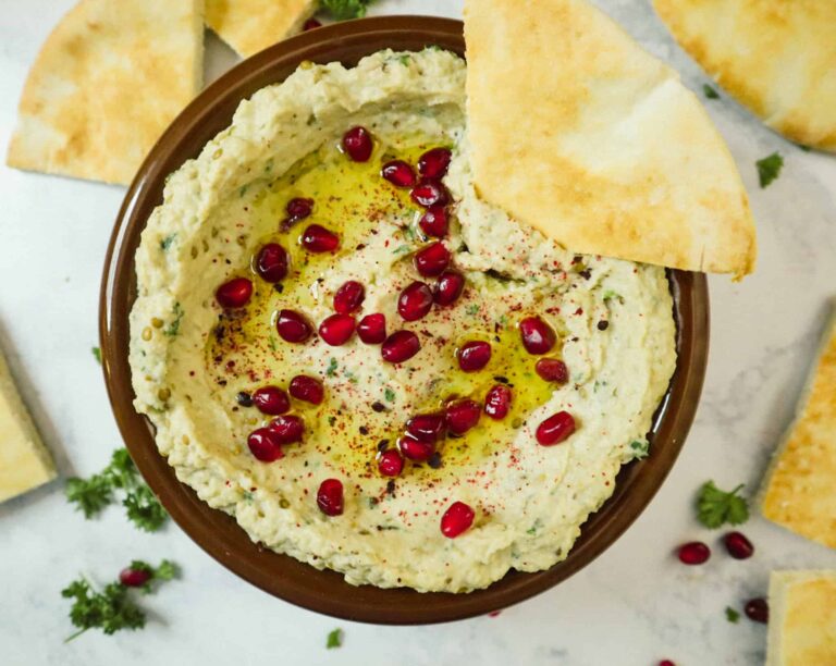 A bowl of a baba ganoush, pomegranate seeds, olive oil, sumac and pieces of pita bread