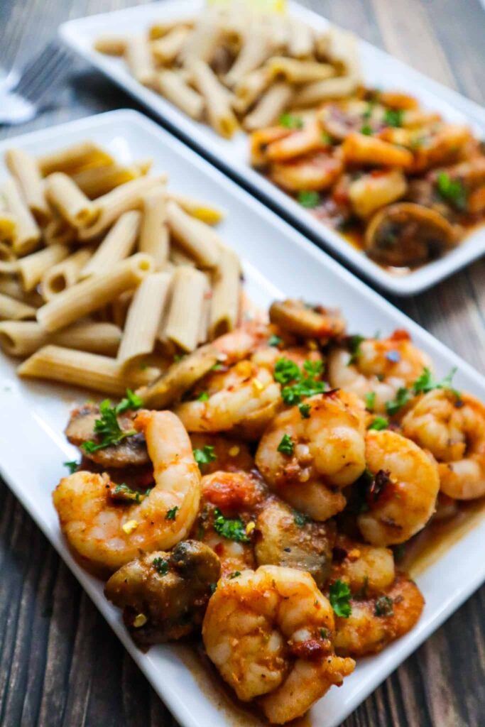 A plate with spicy shrimps and mushrooms with parsley on top and pasta on the side 
