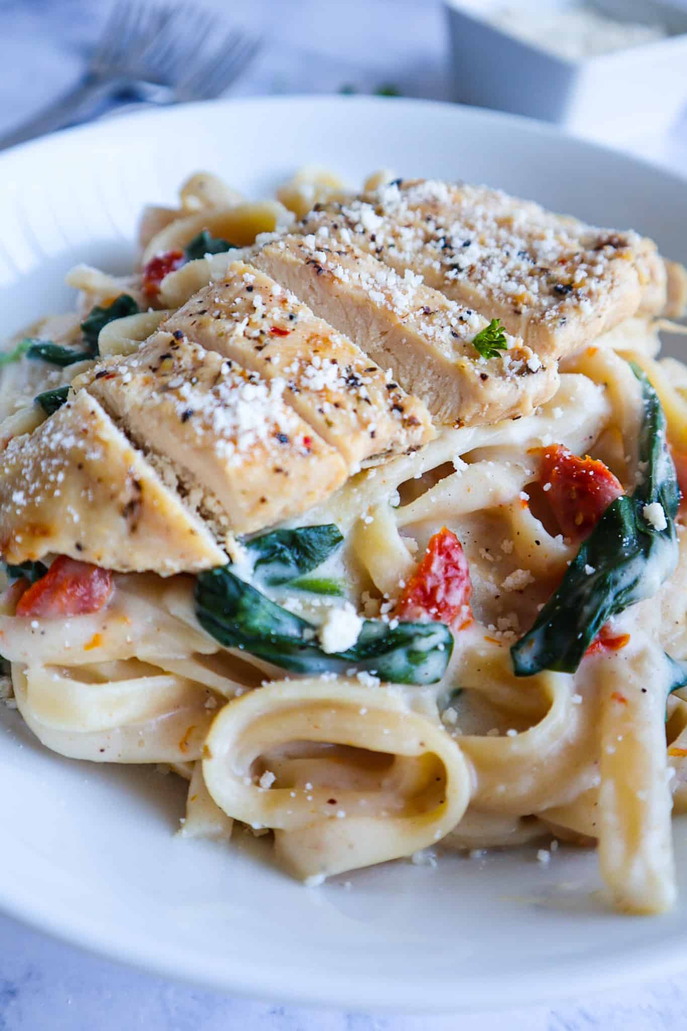 A dish of fettuccine alfredo with grilled chicken, sun dried tomatoes, spinach and parmesan cheese.