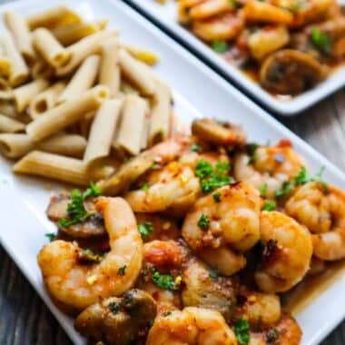 A plate with spicy shrimps and mushrooms with parsley on top and pasta on the side