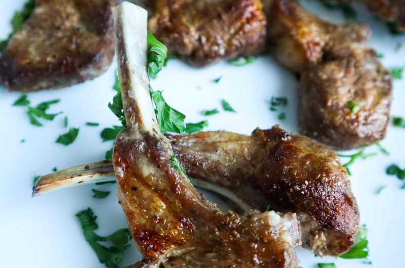 A plate of baked lamb chops with chopped parsley as a garnish