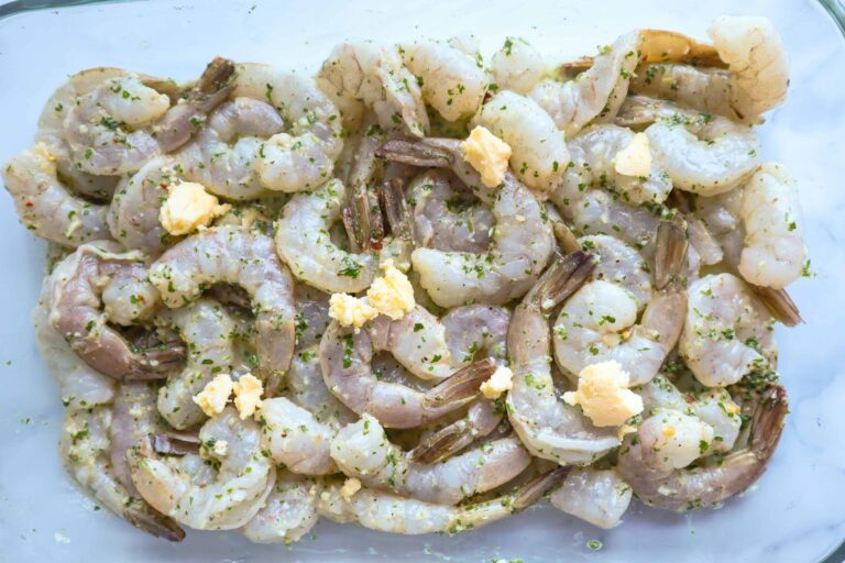Raw Marinated shrimp in an oven tray with butter pieces on top