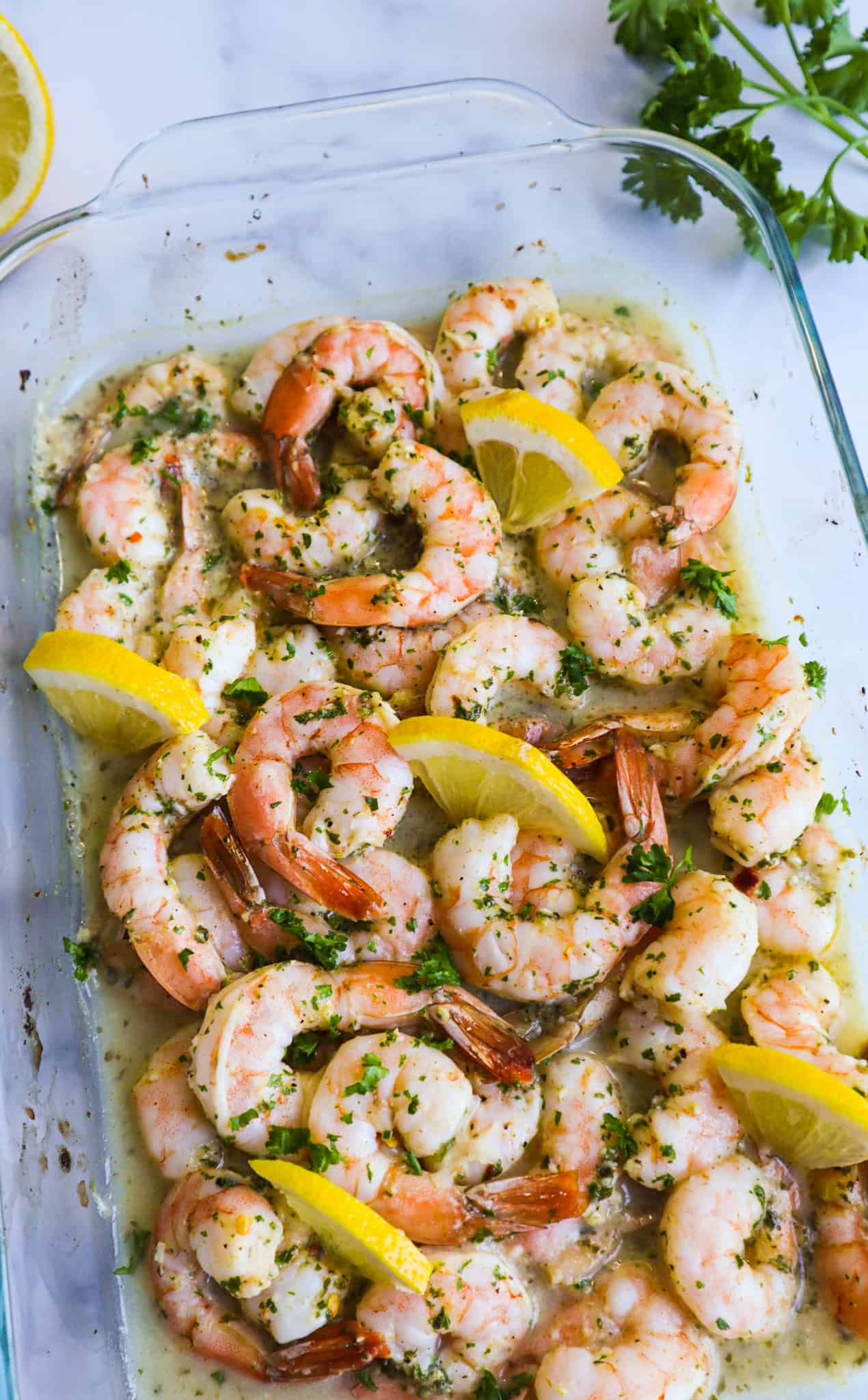 An oven baked shrimp in a pyrex with lemon slices and parsley as garnish