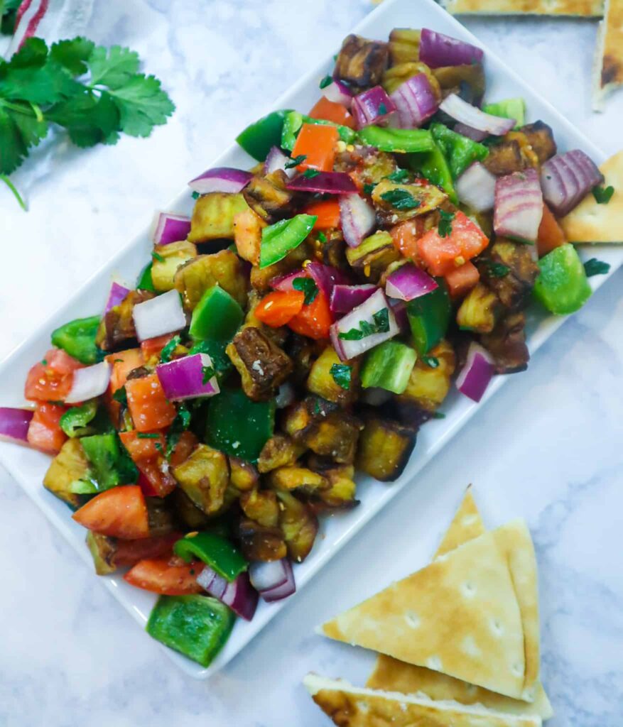 A dish of eggplant salad with veggies and pita bread on the side