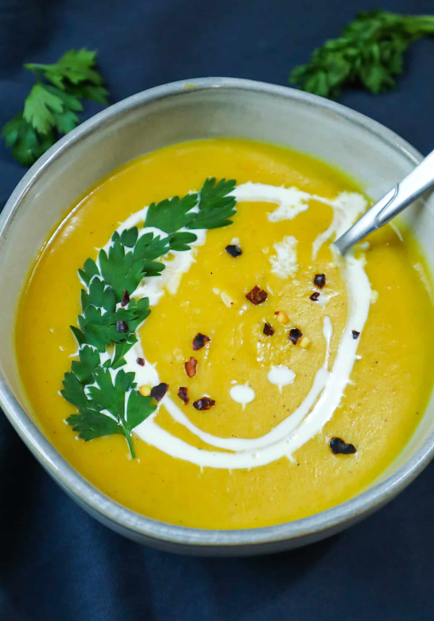 A bowl of pumpkin soup with fresh parsley, chili flakes and drops of heavy cream 