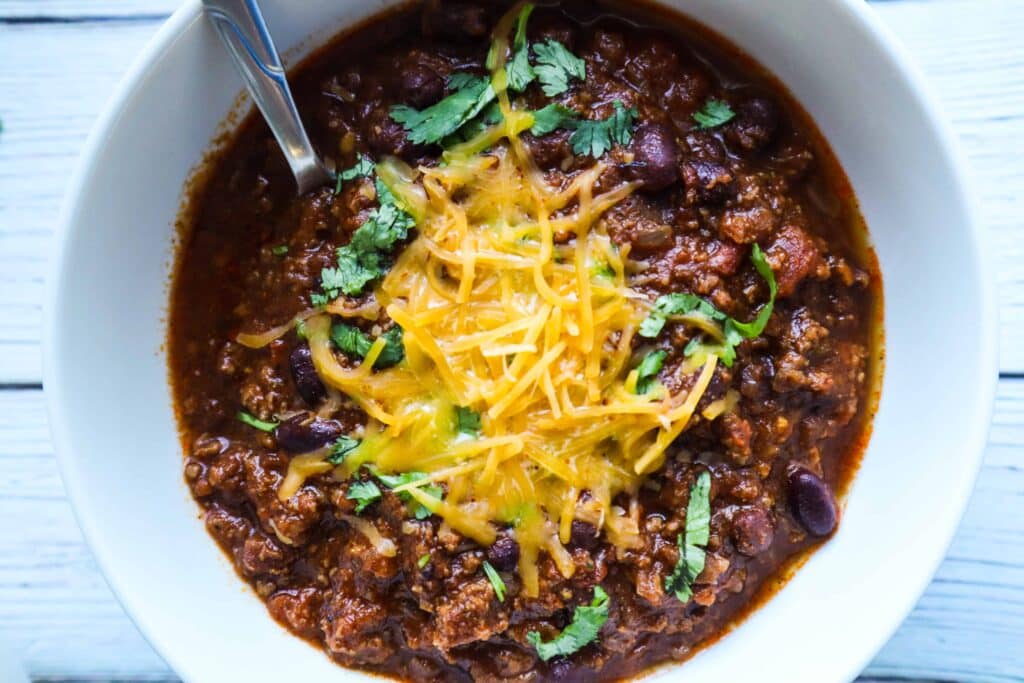 A bowl of chili topped with shredded cheese and chopped cilantro
