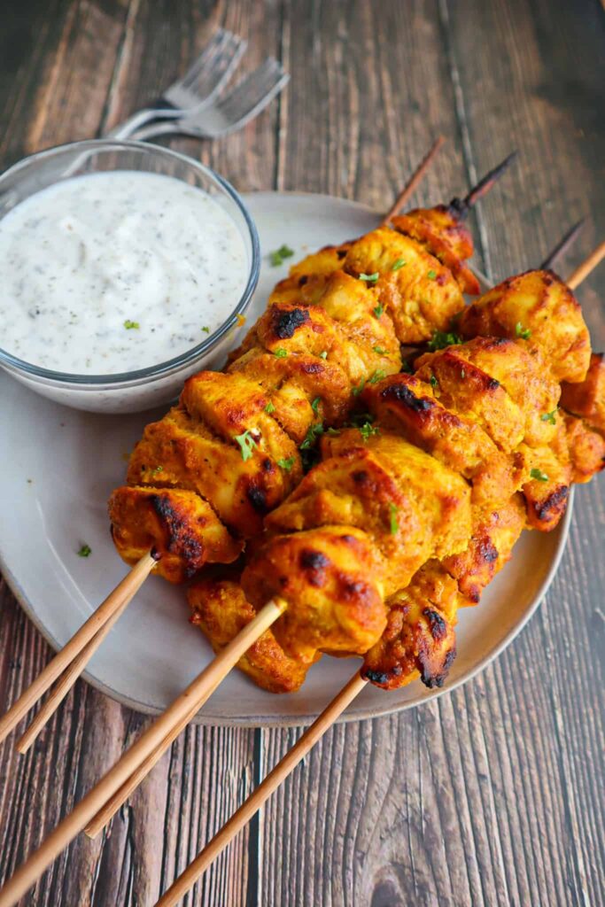 A plate of chicken tandoori skewers and a side of riata.