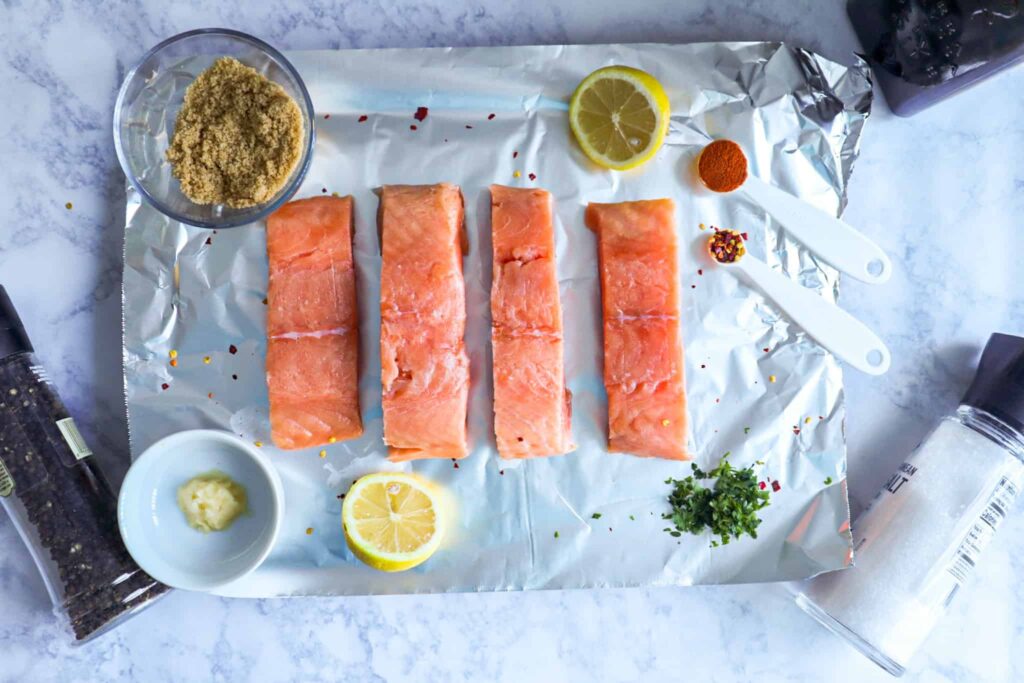 A sheet of aluminum foil, salmon fillets, brown sugar, parsley, lemon, spices and olive oil