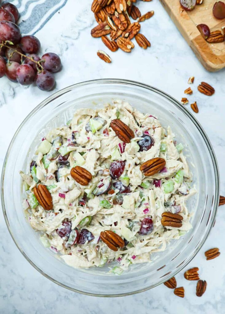 A bowl of chicken salad with pecans on top and sides