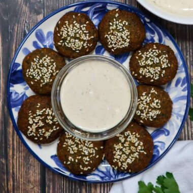 A plate of 8 pieces of falafel with a bowl of tahini sauce in the middle