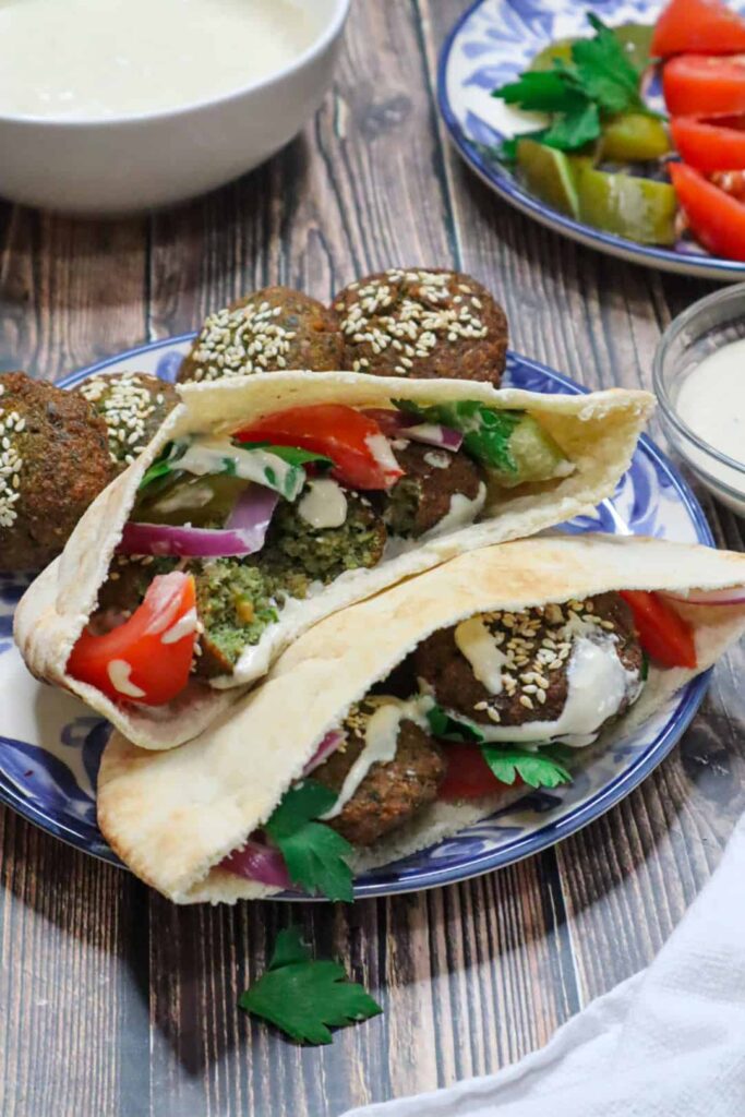 A plate of falafel sandwich with tomatoes, pickles, tahini sauce and parsley 