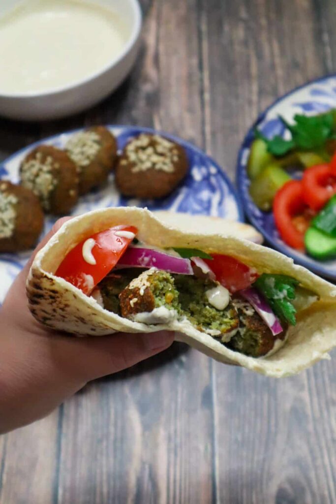 An Egyptian falafel sandwich with tomatoes, pickles, tahini sauce and parsley