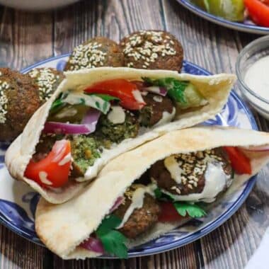 A plate of falafel sandwich with tomatoes, pickles, tahini sauce and parsley