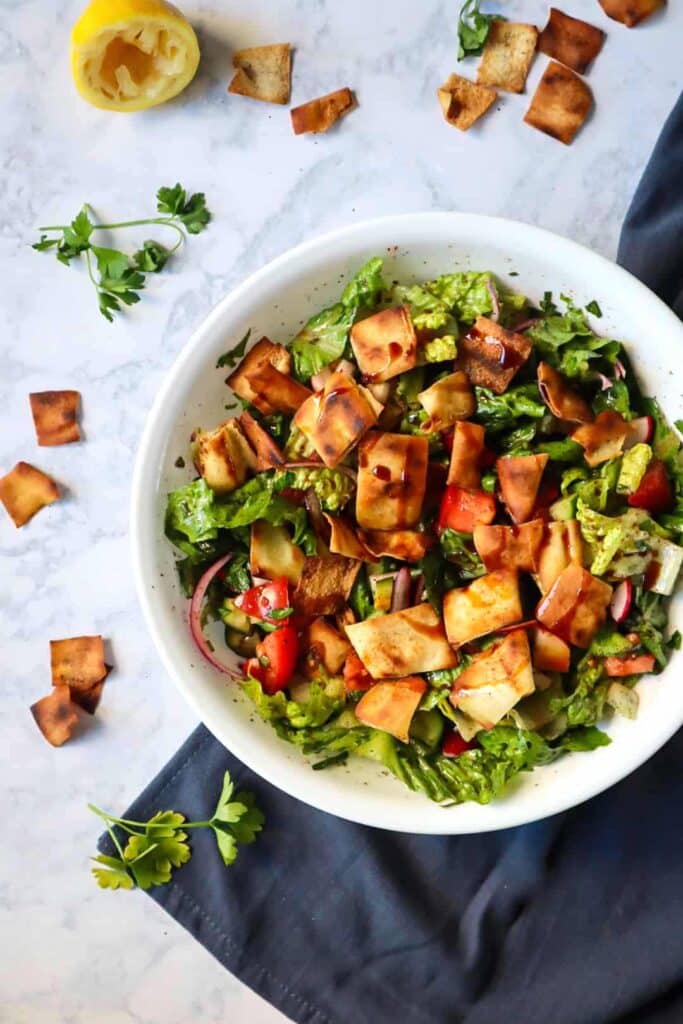 A large bowl of fattoush salad ingredients with pita chips on top and on the side