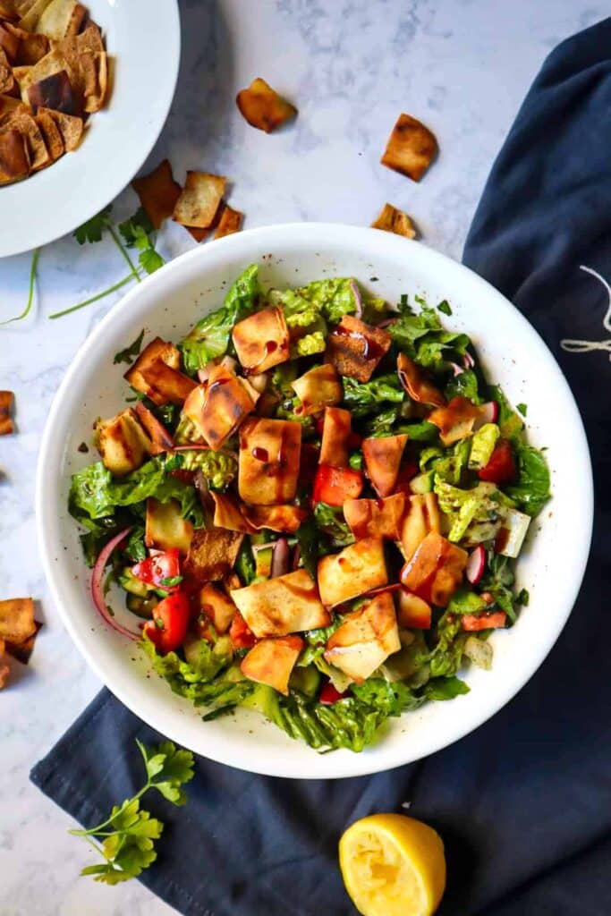 A large bowl of fattoush salad ingredients with pita chips on top and on the side