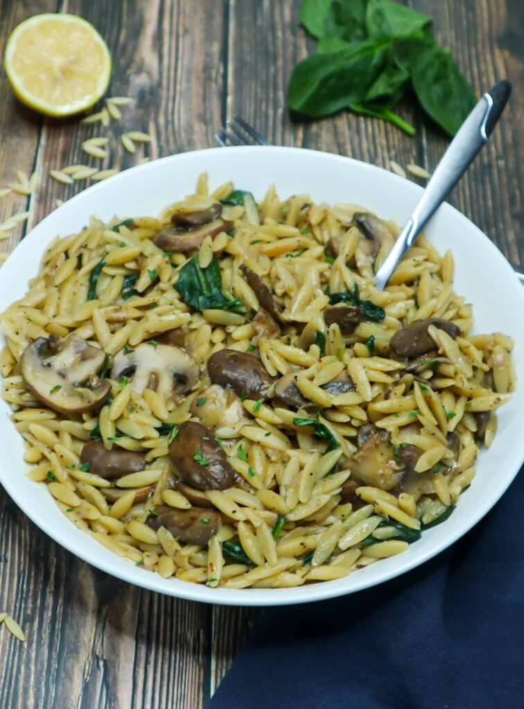 A plate of orzo mushroom with spinach and half a lemon on the side