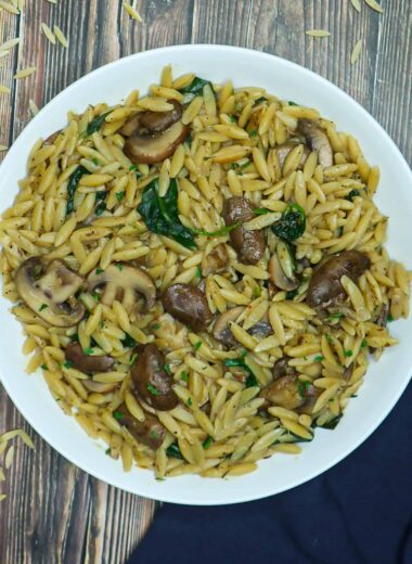 A plate of vegan orzo mushroom with spinach and half a lemon on the side