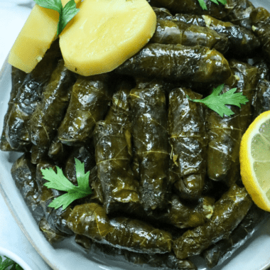 A serving dish of Vegetarian Stuffed Grape Leaves with lemon slices and parsley on the side as a garnish
