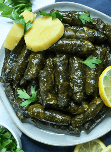 A serving dish of Vegetarian Stuffed Grape Leaves with lemon slices and parsley on the side as a garnish