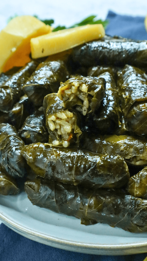 A serving dish of Stuffed Grape Leaves with lemon slices and parsley on the side as a garnish